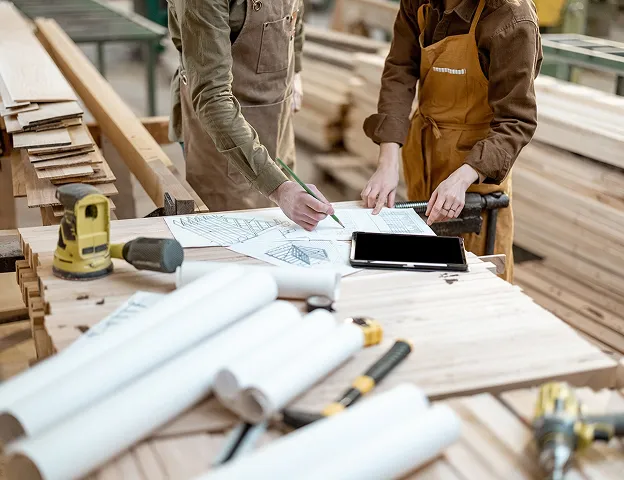 Deux menuisiers examinent des plans et un écran de tablette sur un établi à Croissy-sur-Seine dans les Yvelines 78
