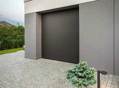 Garage gris foncé avec porte sectionnelle, allée pavée, et petit arbuste vert à Croissy-sur-Seine dans les Yvelines78