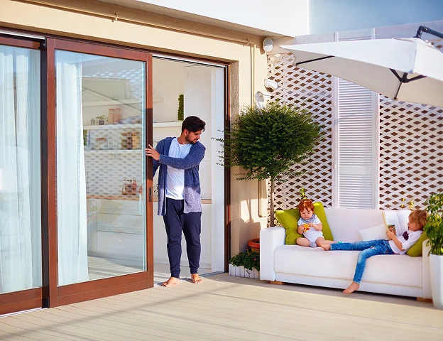 Homme ouvrant une porte coulissante, enfants se détendant sur un canapé sur un balcon à Croissy-sur-Seine dans les Yvelines 78