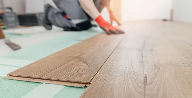 Pose de plancher stratifié marron clair sur sous-couche verte par un ouvrier à Croissy sur Seine dans les Yvelines 78